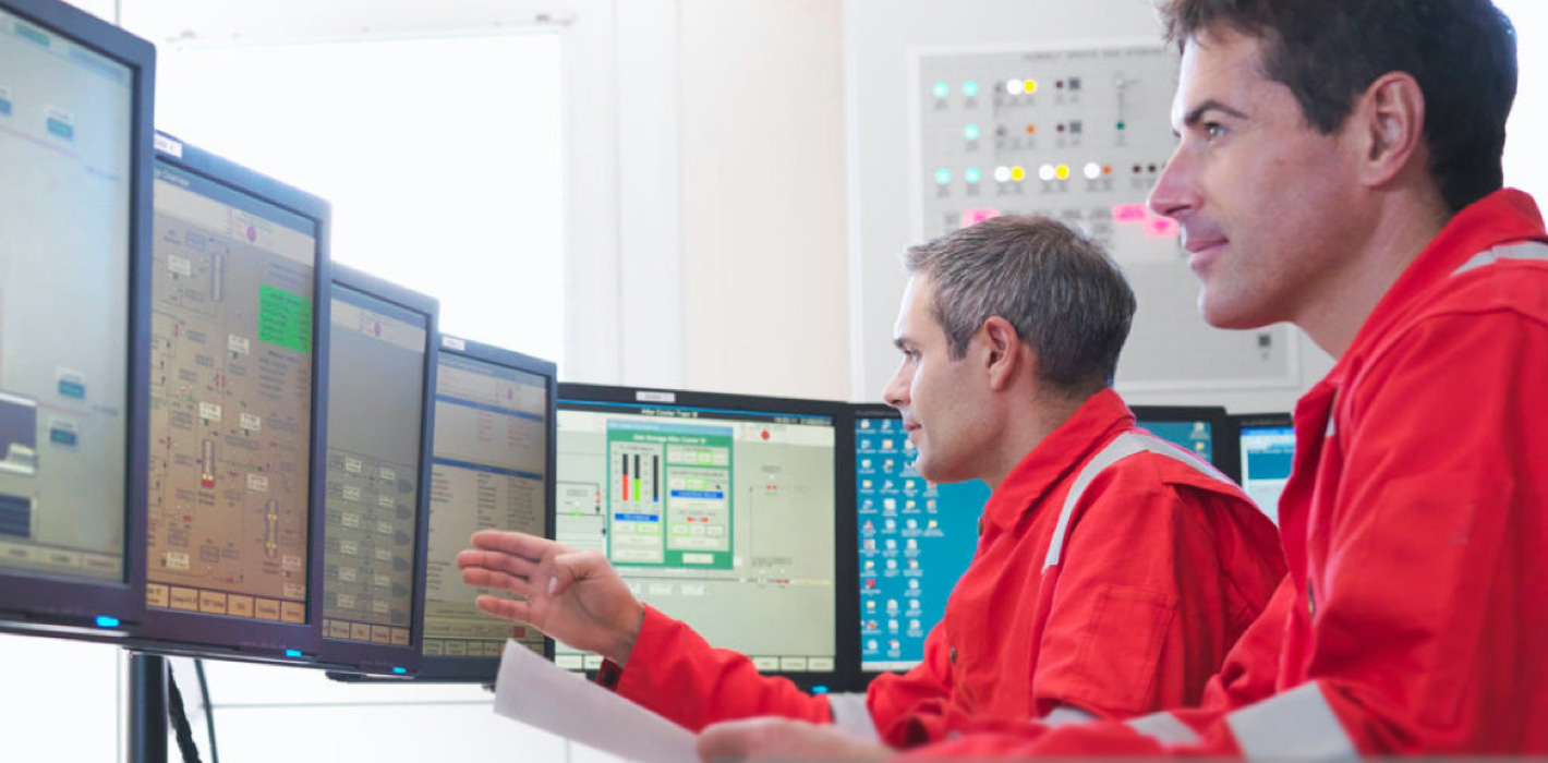 Two men with red uniform watching data on multiple monitors