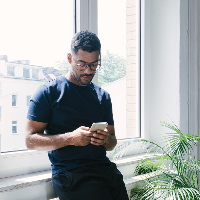 An adult man staying near the window while he's navigating on his phone